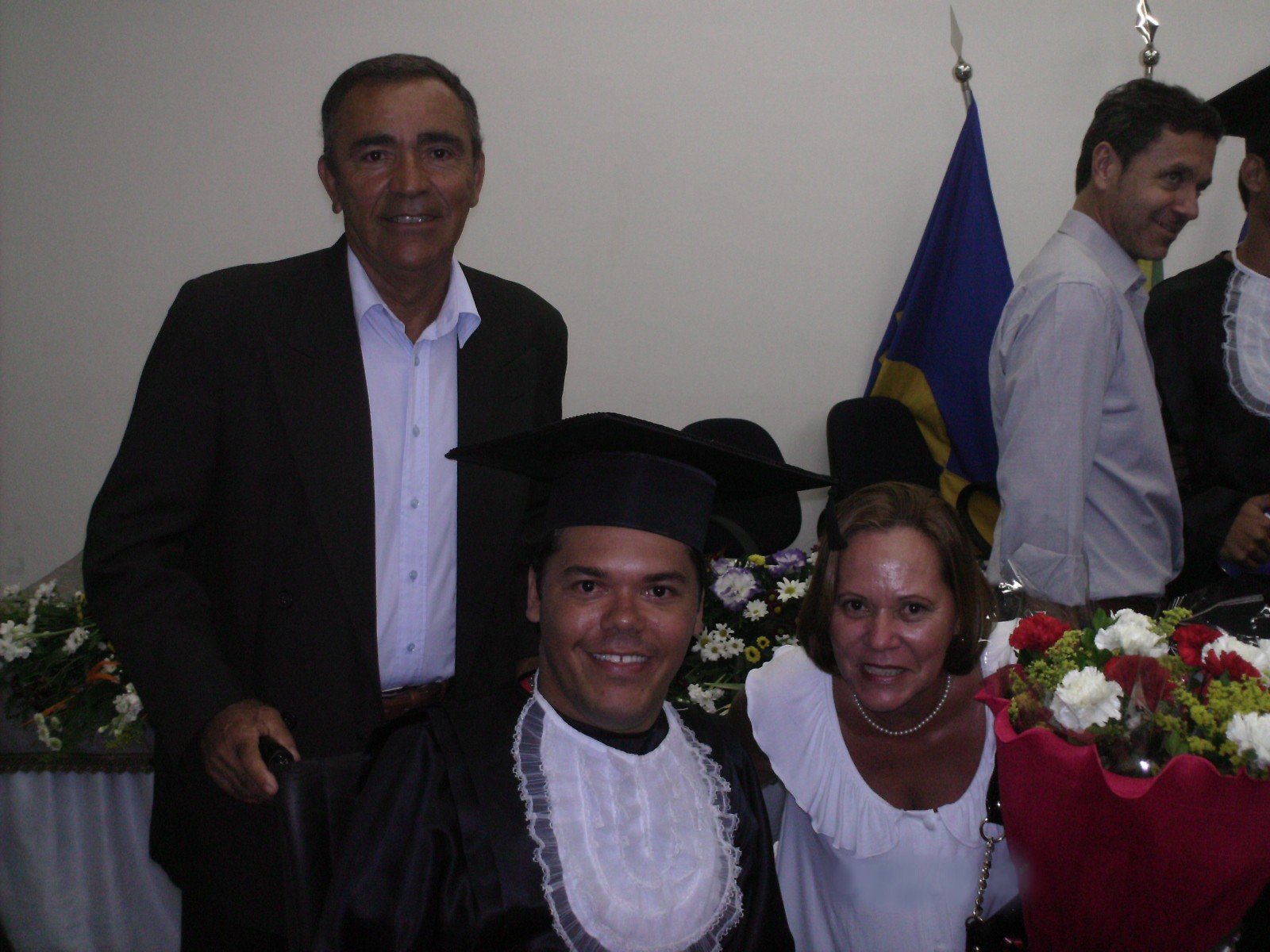 Sidney Reis Borges de beca e capelo no dia da formatura, entre duas pessoas.